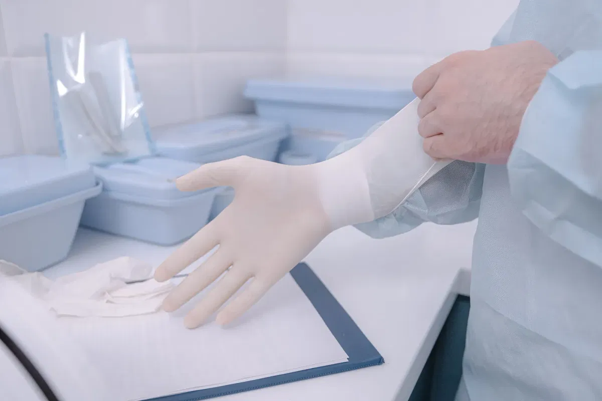 Clinician pulling a white vinyl examination glove onto the hand in a clinic