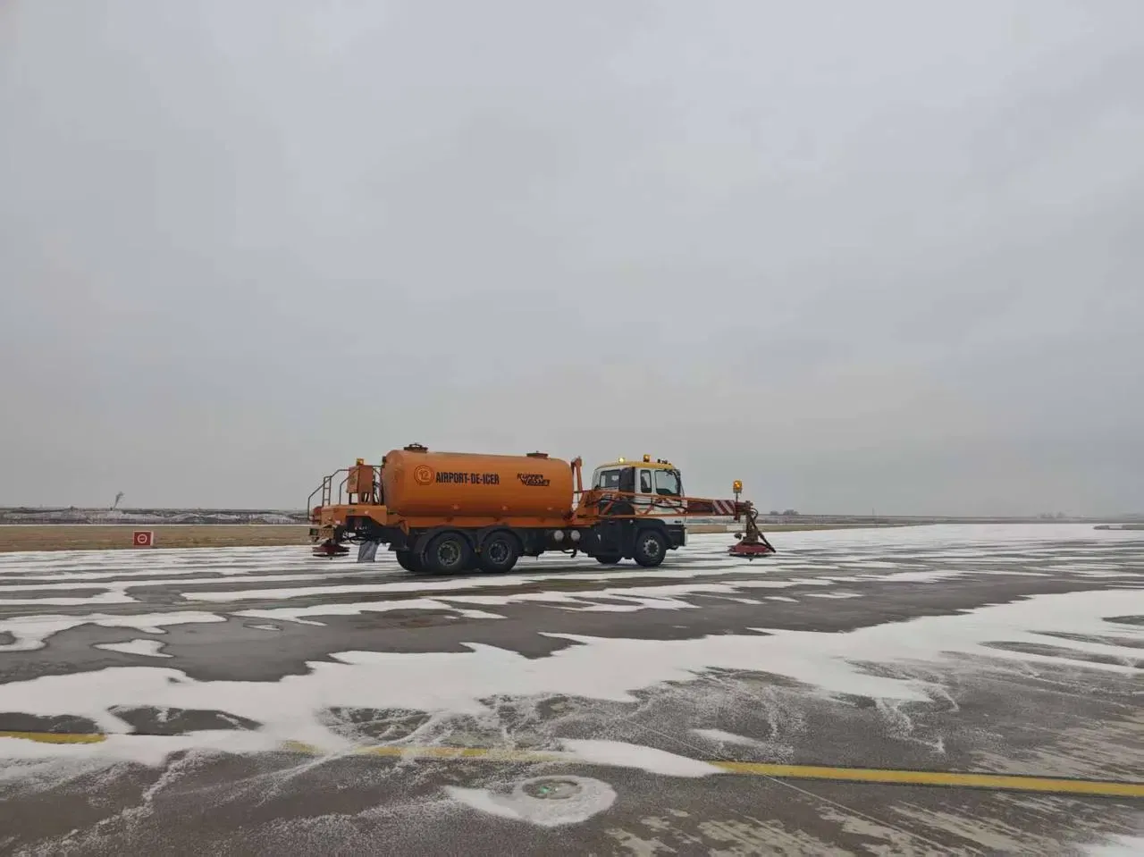 Runway deicing truck applying MEG-based deicing fluid on airport taxiway in winter
