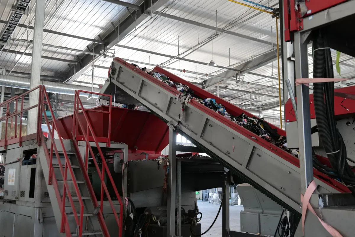 Inclined conveyor carrying mixed waste PET and textile feedstock into the recycling line at the Wansheng plant