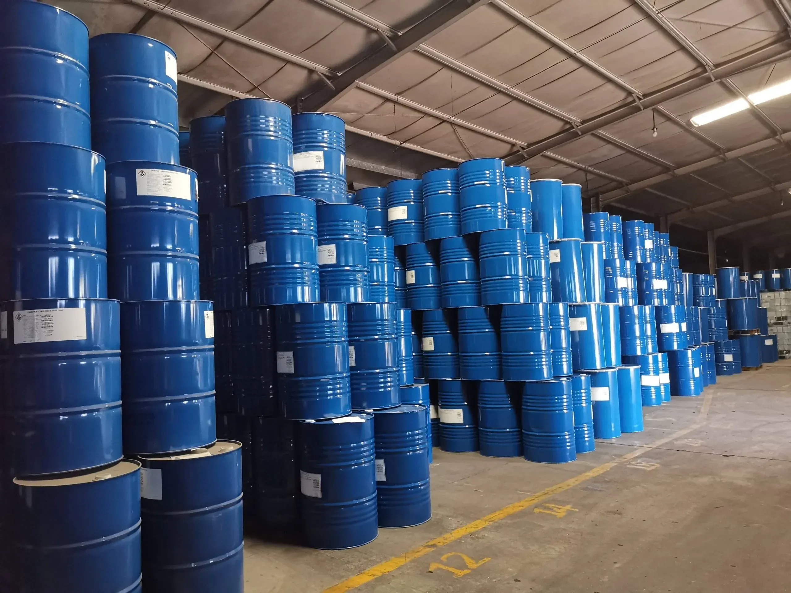 High-bay warehouse with tall stacks of blue chemical barrels